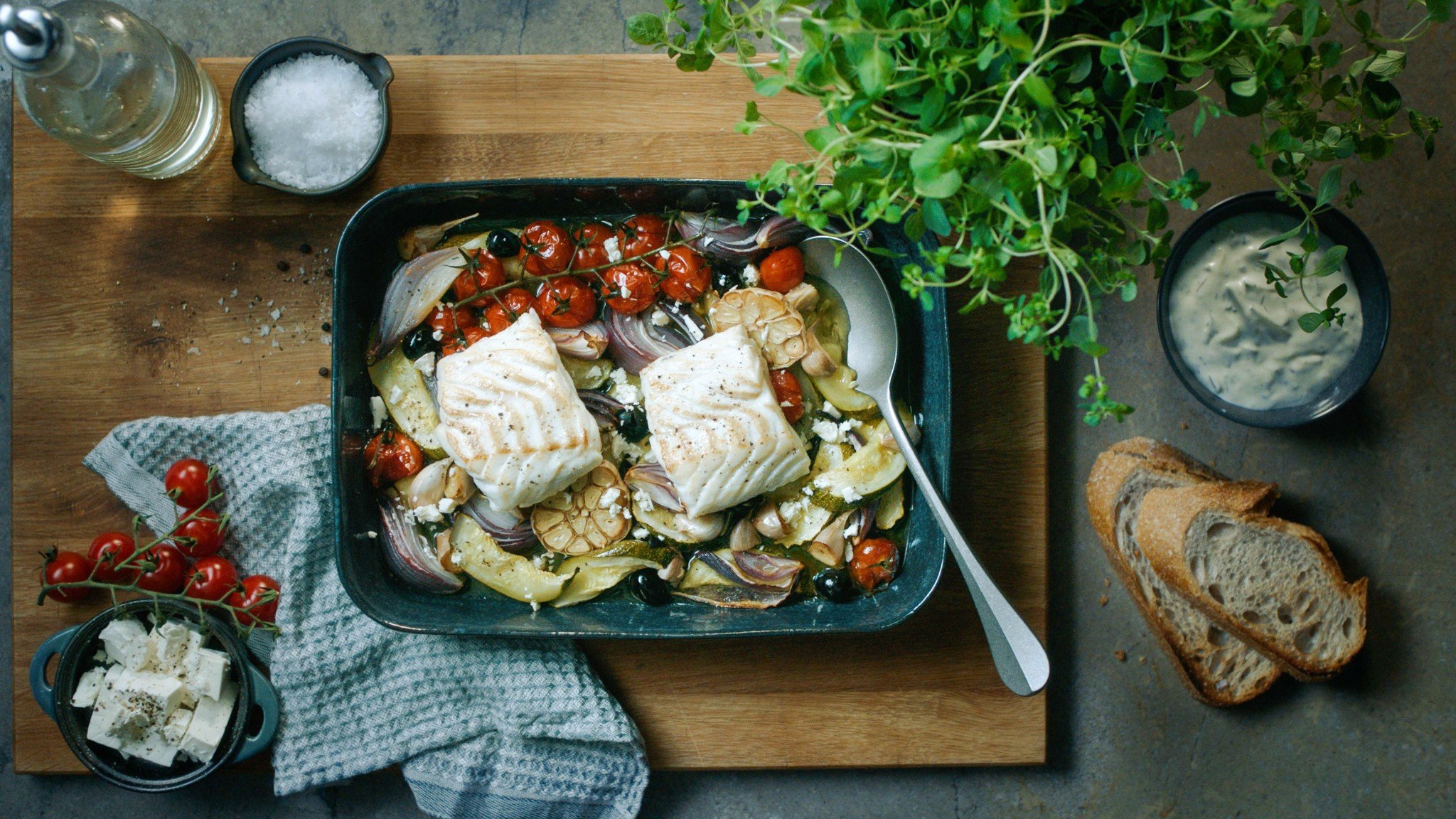 Baked Norwegian cod fillets with cherry tomatoes, olives, red onion and feta in an oven dish.