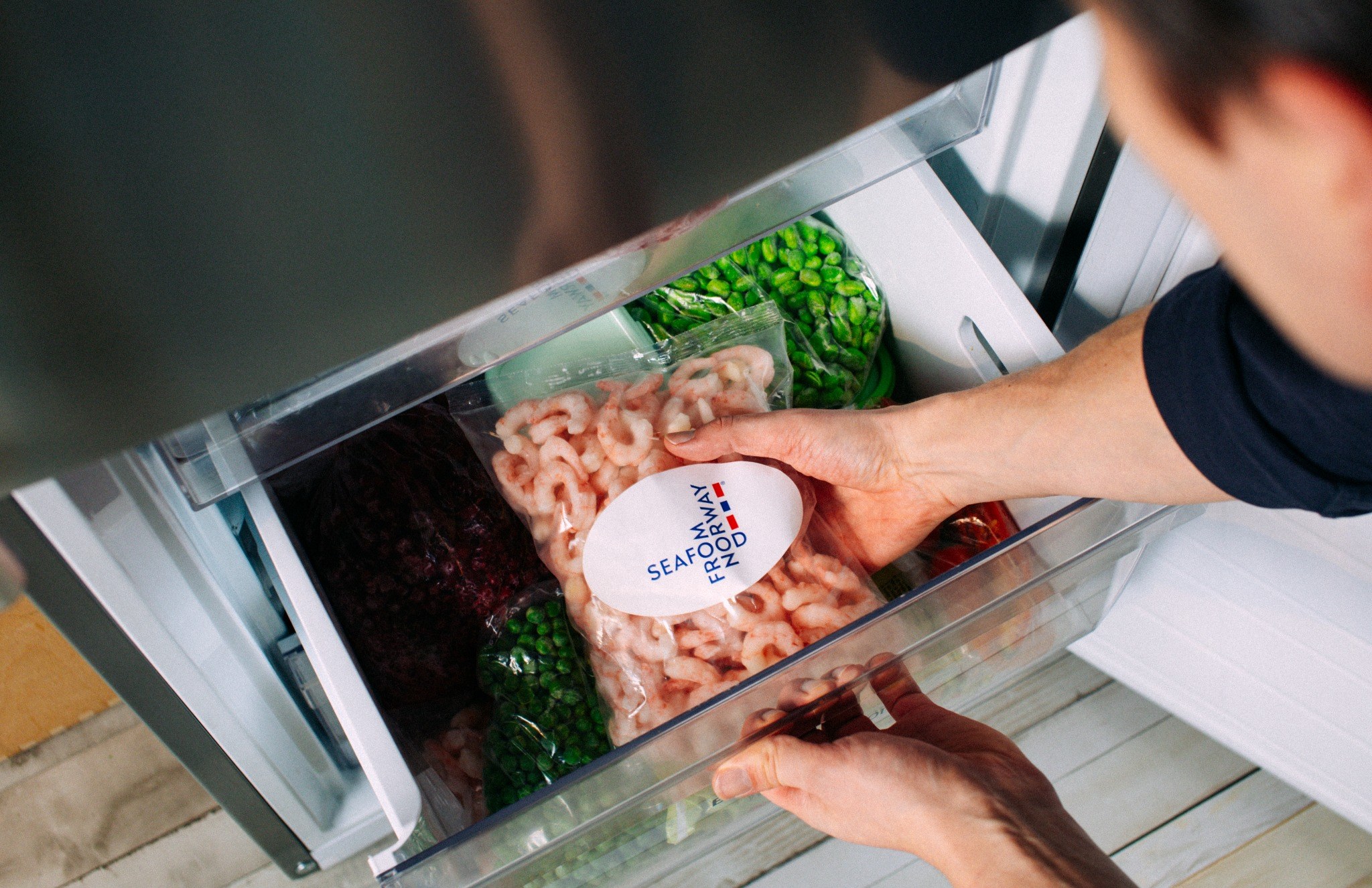 A shopper takes a bag of frozen Norwegian cold-water prawns labelled Seafood from Norway out of a freezer drawer.